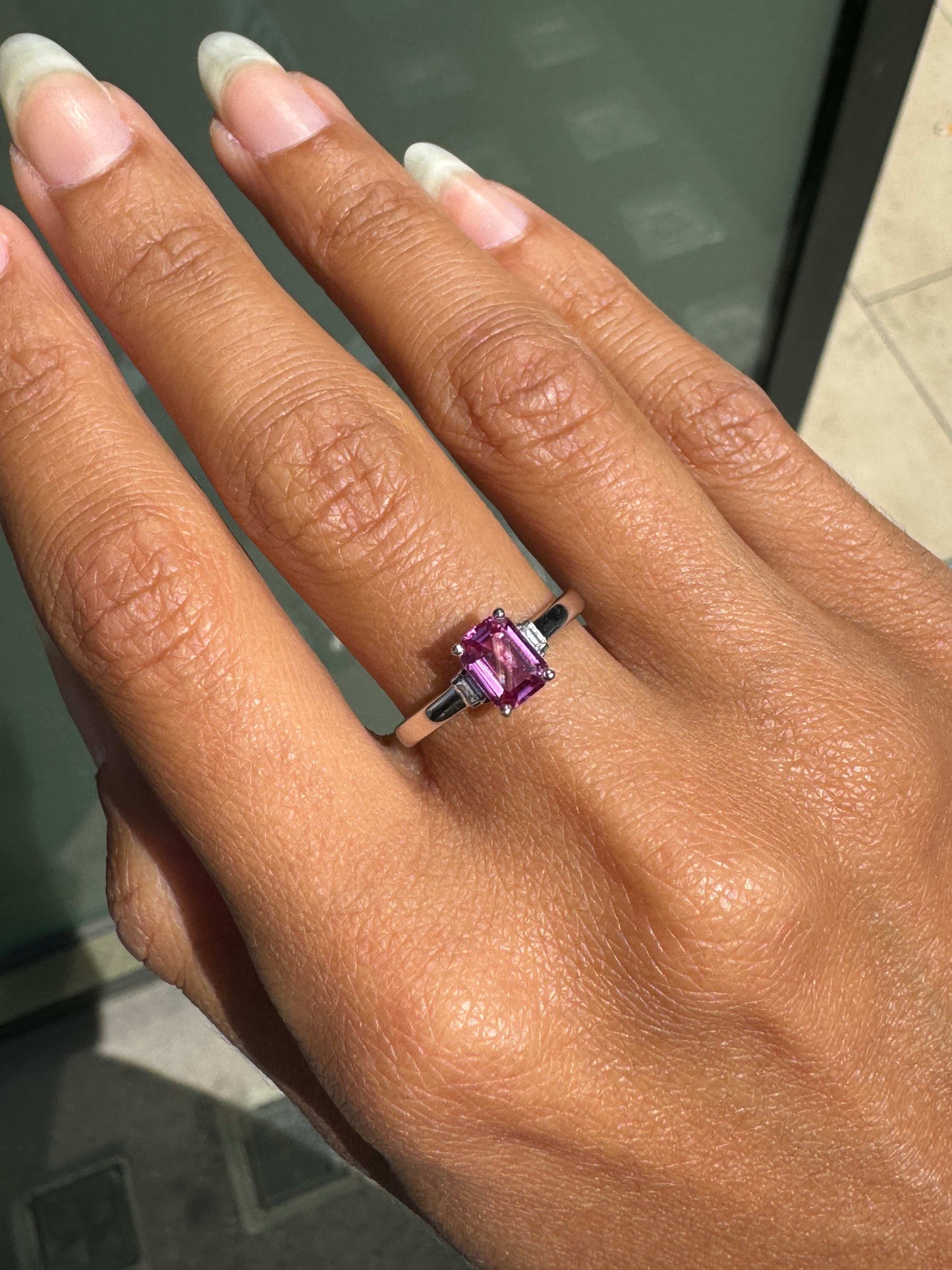 Hand wearing a ring with a pink sapphire on a neutral background