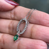 An 18 carat white gold oval pendant featuring a central emerald, surrounded by round brilliant cut diamonds set in a claw-like design.