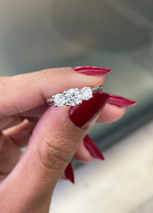 A platinum engagement ring with a central round brilliant cut diamond and two smaller round cut diamonds on the sides, set in an open work gallery.