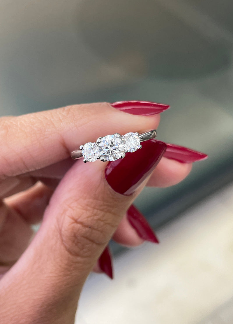 A platinum engagement ring with a central round brilliant cut diamond and two smaller round cut diamonds on the sides, set in an open work gallery.