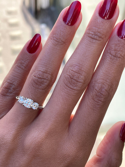 A platinum engagement ring with a central round brilliant cut diamond and two smaller round cut diamonds on the sides, set in an open work gallery on hand.