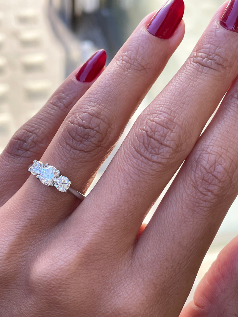 A platinum engagement ring with a central round brilliant cut diamond and two smaller round cut diamonds on the sides, set in an open work gallery on hand.