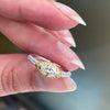 A marquise diamond engagement ring with an east west setting  halo of round yellow diamonds set in rose gold, with smaller white round brilliant cut diamonds set in a contrasting band of platinum. side view