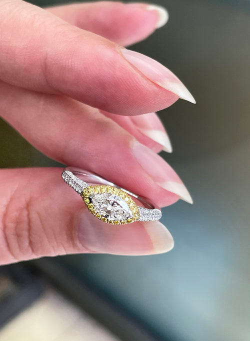 A marquise diamond engagement ring with an east west setting  halo of round yellow diamonds set in rose gold, with smaller white round brilliant cut diamonds set in a contrasting band of platinum. side view