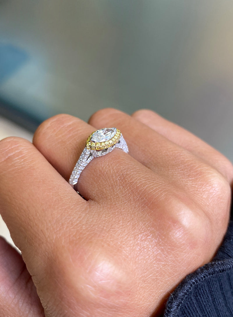 A marquise diamond engagement ring with an east west setting  halo of round yellow diamonds set in rose gold, with smaller white round brilliant cut diamonds set in a contrasting band of platinum. side view
