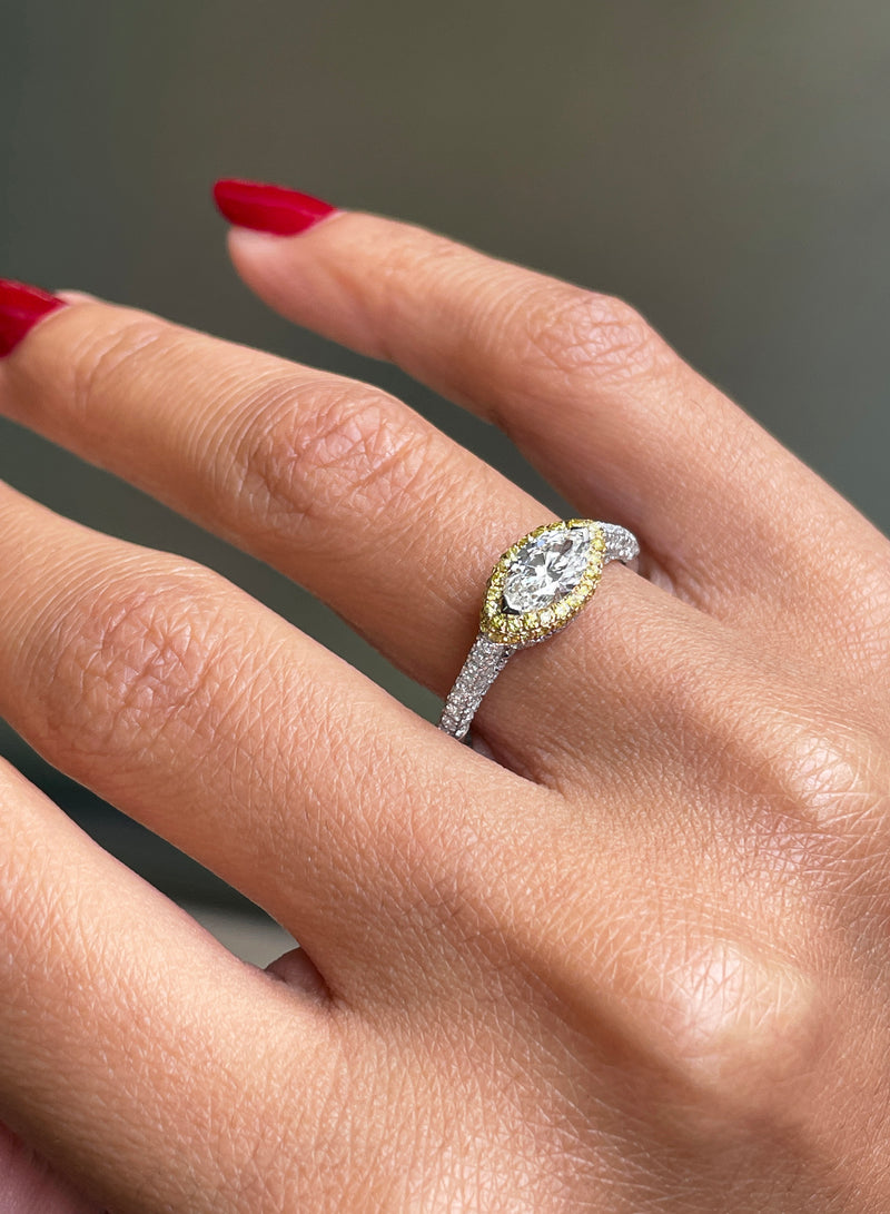 A marquise diamond engagement ring with an east west setting  halo of round yellow diamonds set in rose gold, with smaller white round brilliant cut diamonds set in a contrasting band of platinum. side view