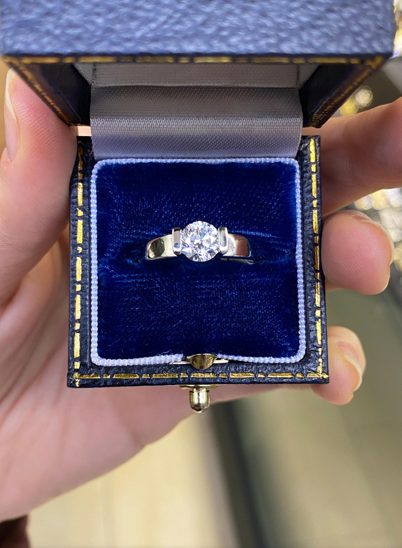 A white gold engagement ring with a round brilliant cut diamond centerpiece, set in a tapered platinum band in box