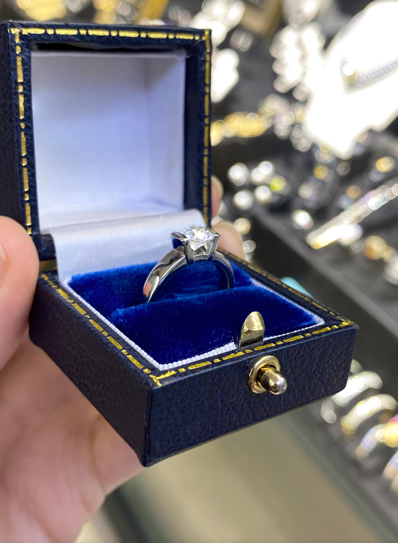 A white gold engagement ring with a round brilliant cut diamond centerpiece, set in a tapered platinum band in box