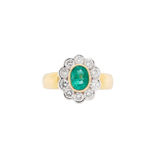 An oval emerald ring with a diamond halo, set in a cluster design with yellow and white gold.