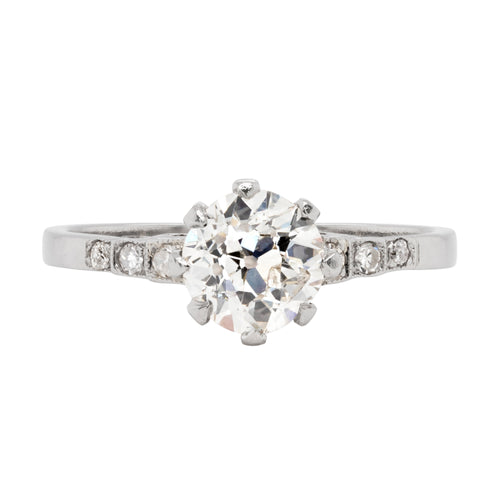 Antique engagement ring with a central old cut diamond and smaller diamonds on the sides, set in a platinum mounting with an open back design.