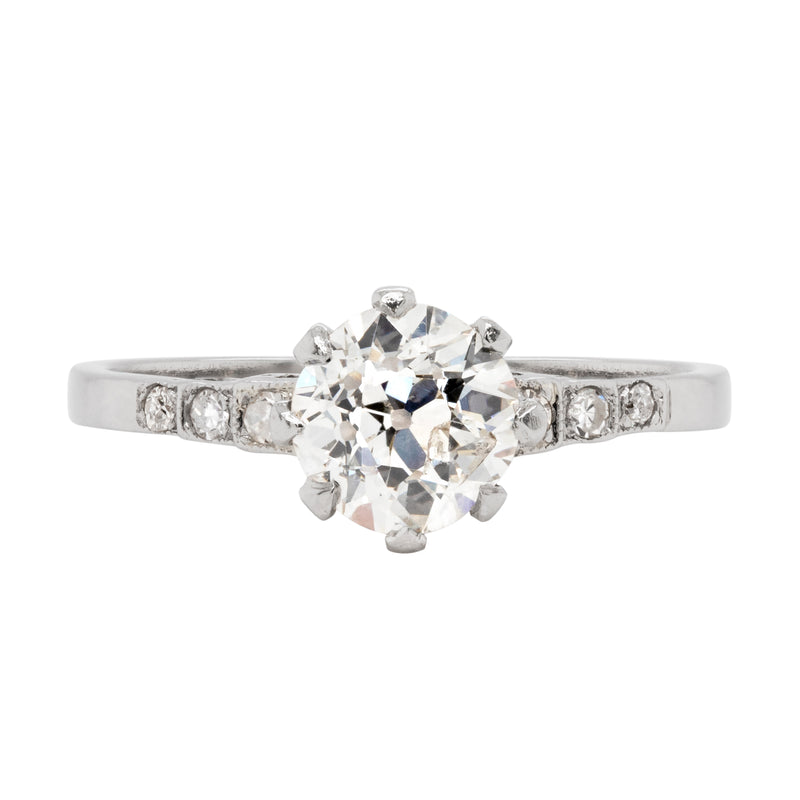Antique engagement ring with a central old cut diamond and smaller diamonds on the sides, set in a platinum mounting with an open back design.
