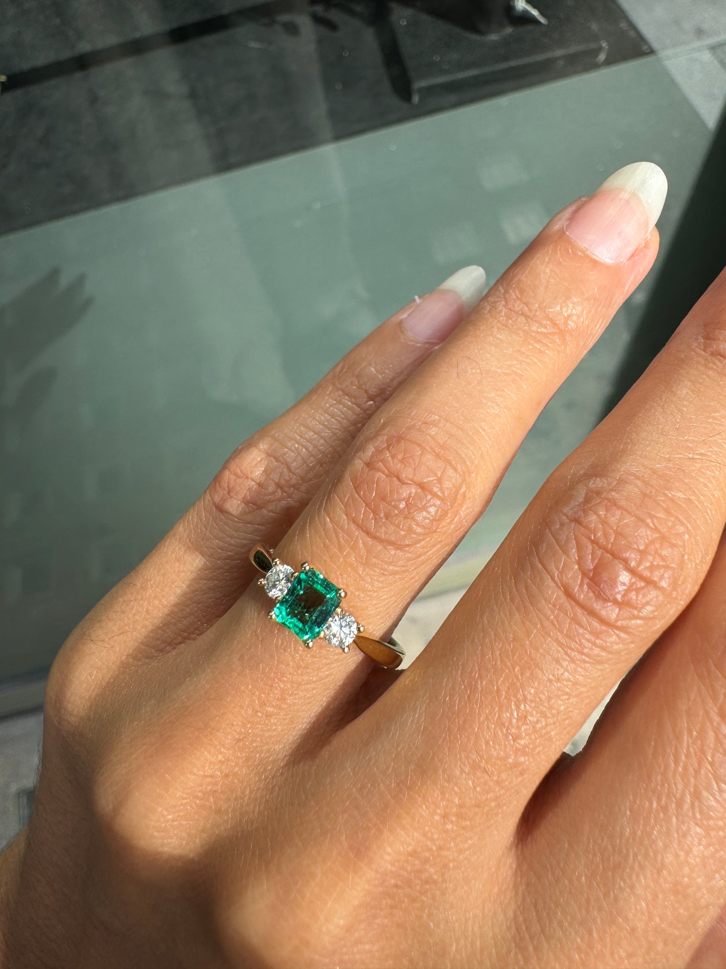 Hand wearing a ring with a green gemstone on a reflective surface