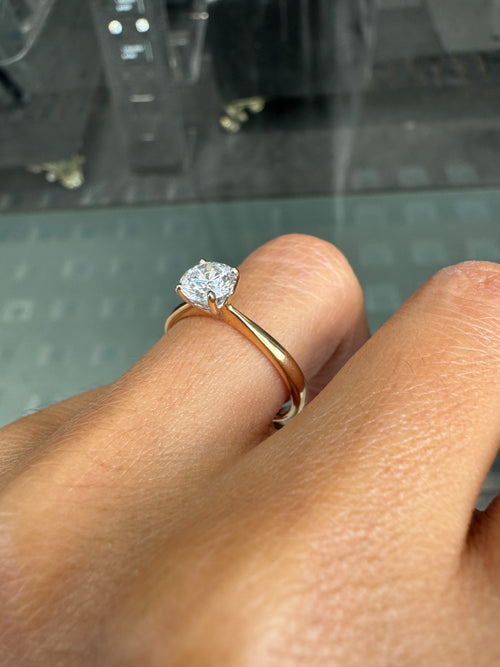 Close-up of a hand wearing a gold ring with a diamond on a blurred background