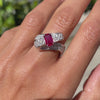 18ct white gold twisted ribbon dress ring with 1.04ct emerald cut ruby centre and 1.30ct round brilliant cut diamonds inlaid in two rows on hand