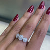 An 18 carat white gold trilogy diamond cluster engagement ring with three circular diamond clusters and a princess cut diamond in the center, set in a white gold band on hand
