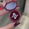An antique engagement ring featuring a central diamond, flanked by two smaller diamonds and a pearl, all set in platinum on a rose gold mount in box