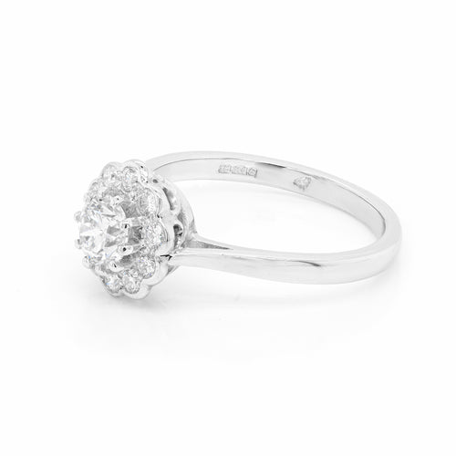 side view of a round brilliant cut diamond ring with smaller round brilliant cut diamonds set in a daisy cluster design, mounted in a platinum band.