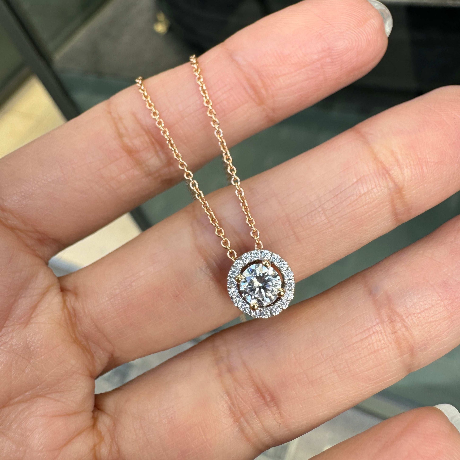An 18 carat rose gold halo cluster pendant featuring a round brilliant cut diamond center stone with a halo of smaller round diamonds, suspended on a slender gold chain. on hand
