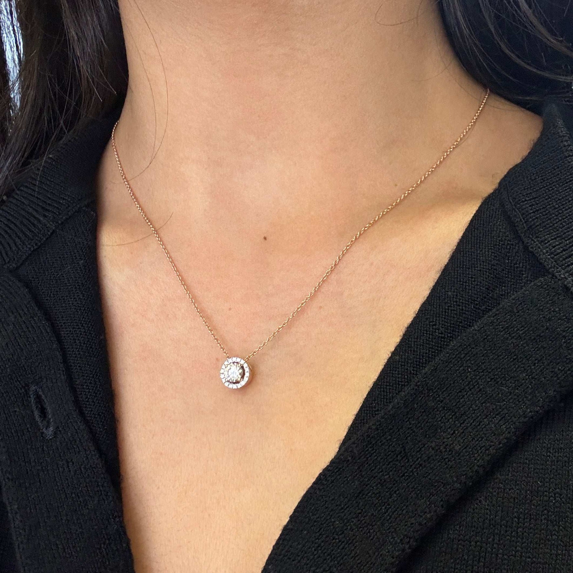 An 18 carat rose gold halo cluster pendant featuring a round brilliant cut diamond center stone with a halo of smaller round diamonds, suspended on a slender gold chain. on neck