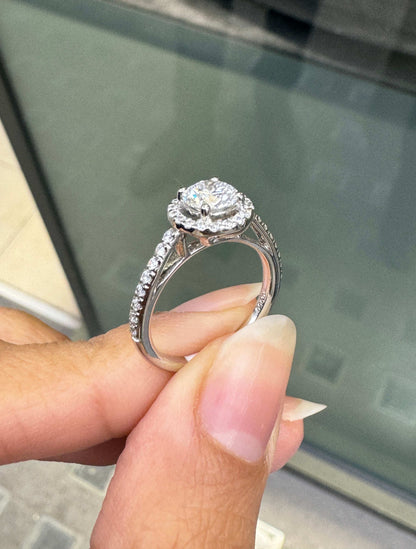 0.70ct E VS1 diamond halo cluster engagement ring in platinum with round brilliant cut centre stone, halo and diamond shoulders on hand