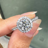 0.70ct E VS1 diamond halo cluster engagement ring in platinum with round brilliant cut centre stone, halo and diamond shoulders on hand 