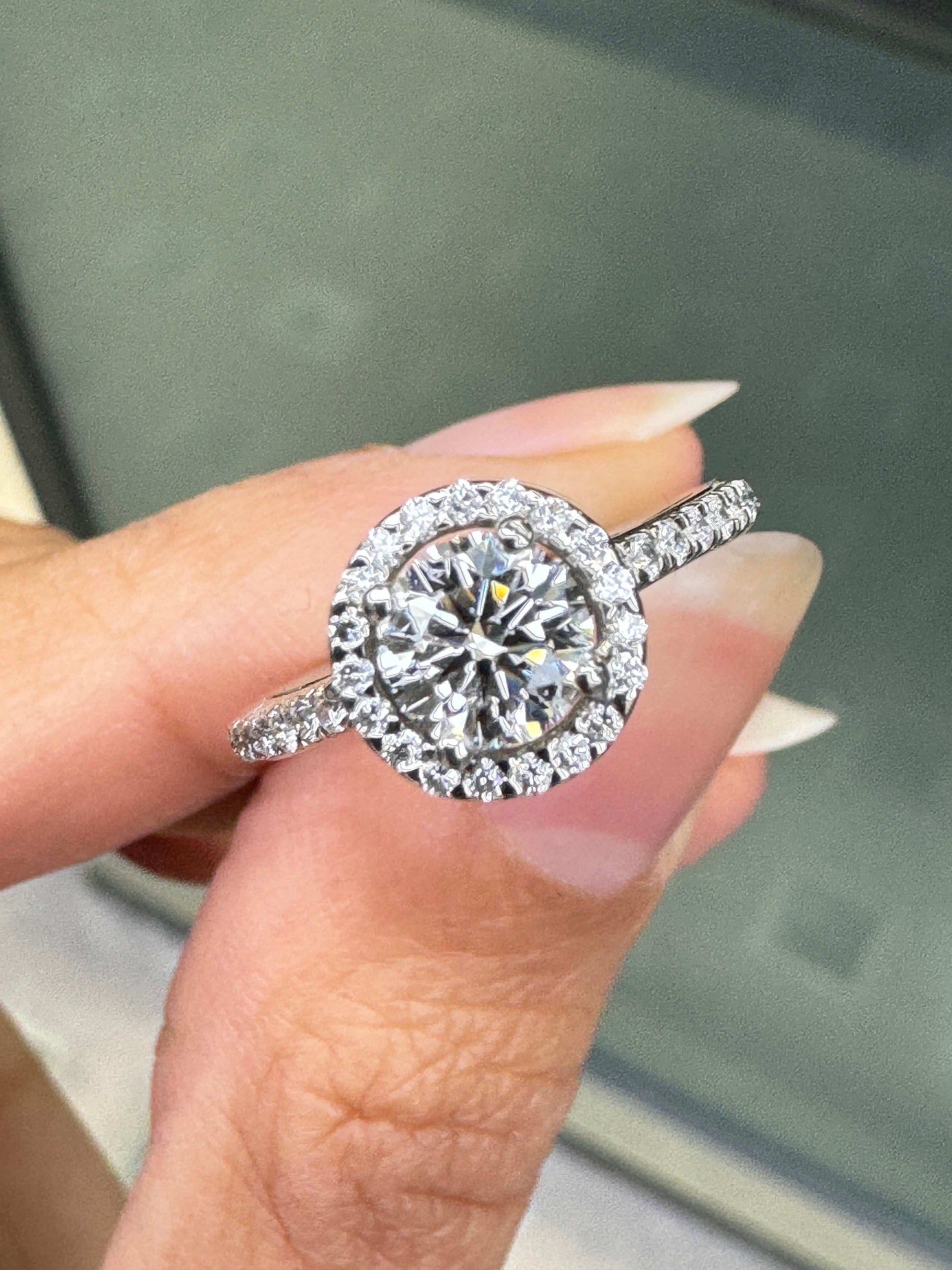 0.70ct E VS1 diamond halo cluster engagement ring in platinum with round brilliant cut centre stone, halo and diamond shoulders on hand 