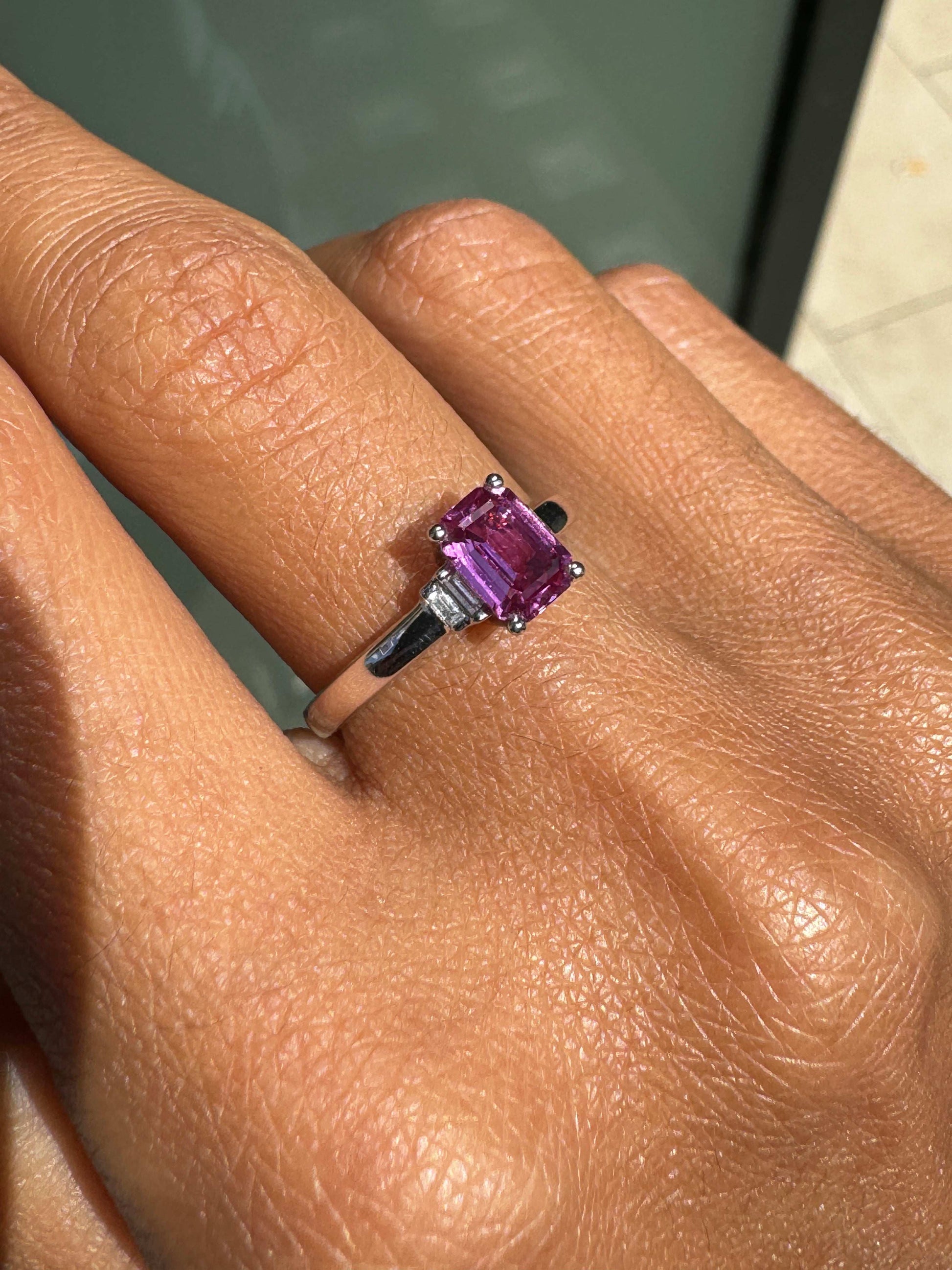 pink sapphire ring on a finger with a blurred background
