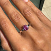 Hand wearing a ring with a pink sapphire on a neutral background