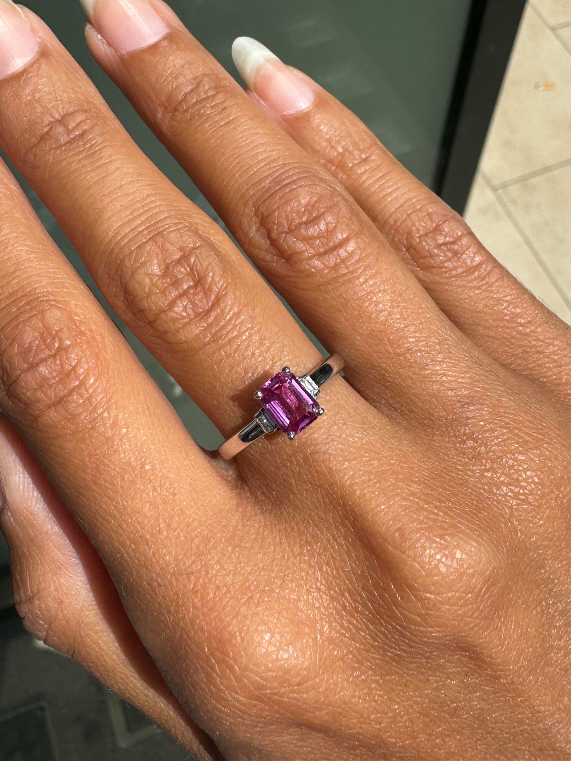 Hand wearing a ring with a pink sapphire on a neutral background