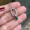 An 18 carat white gold oval pendant featuring a central emerald, surrounded by round brilliant cut diamonds set in a claw-like design.