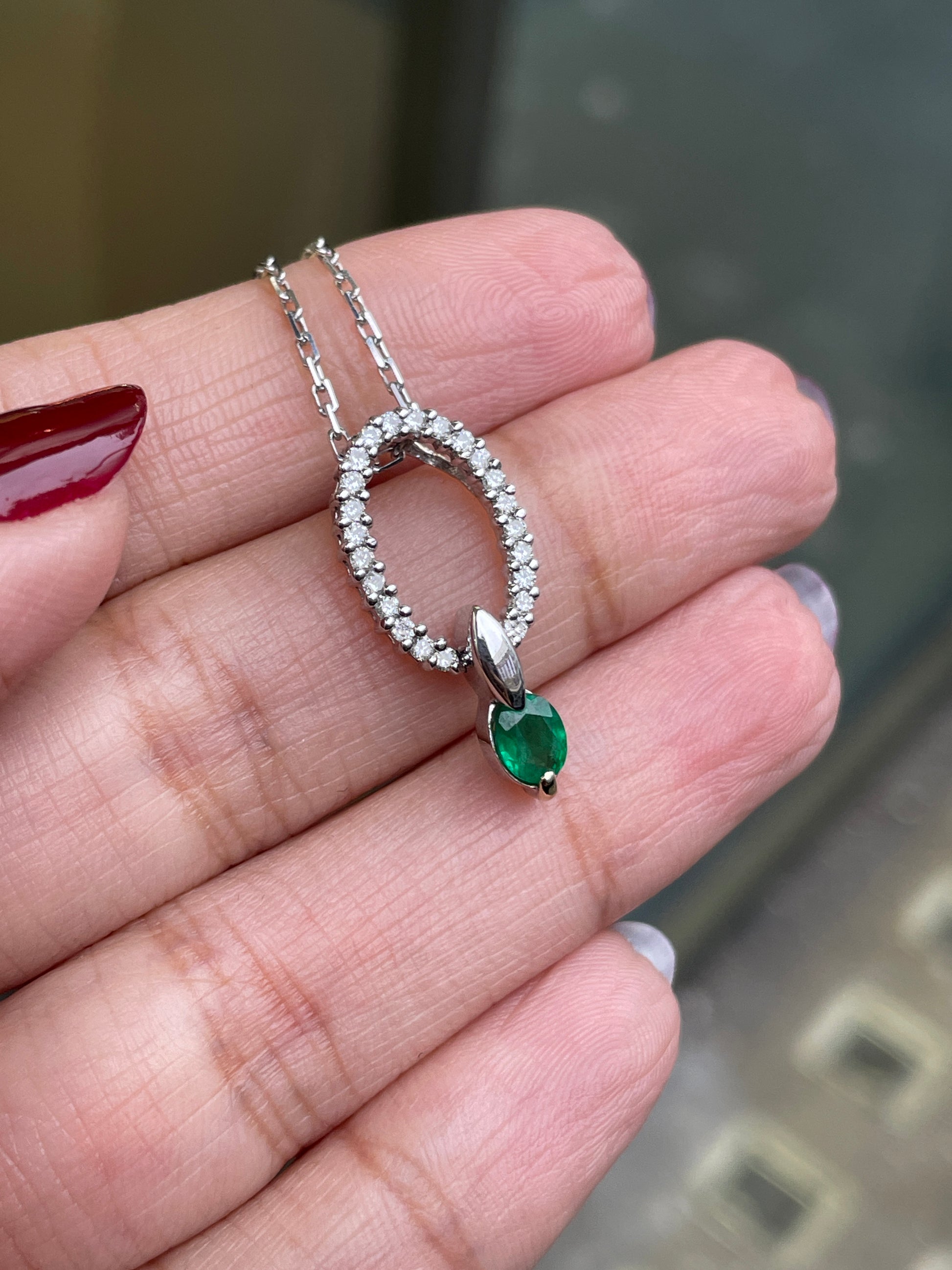 An 18 carat white gold oval pendant featuring a central emerald, surrounded by round brilliant cut diamonds set in a claw-like design.