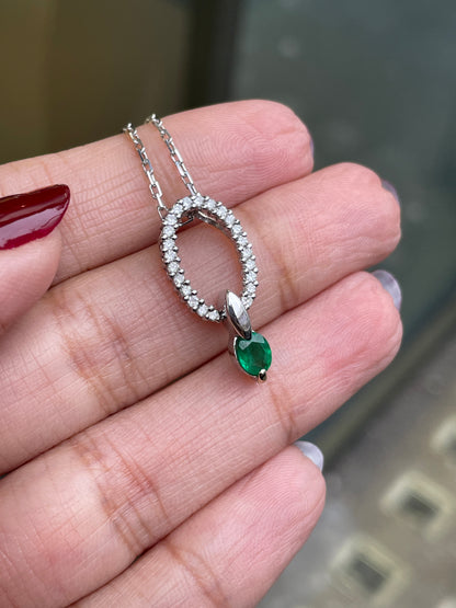 An 18 carat white gold oval pendant featuring a central emerald, surrounded by round brilliant cut diamonds set in a claw-like design.