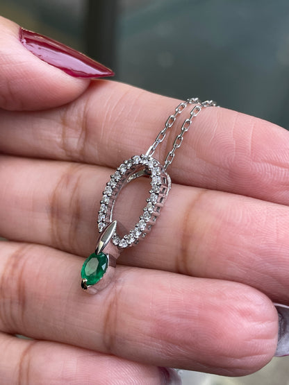 An 18 carat white gold oval pendant featuring a central emerald, surrounded by round brilliant cut diamonds set in a claw-like design.