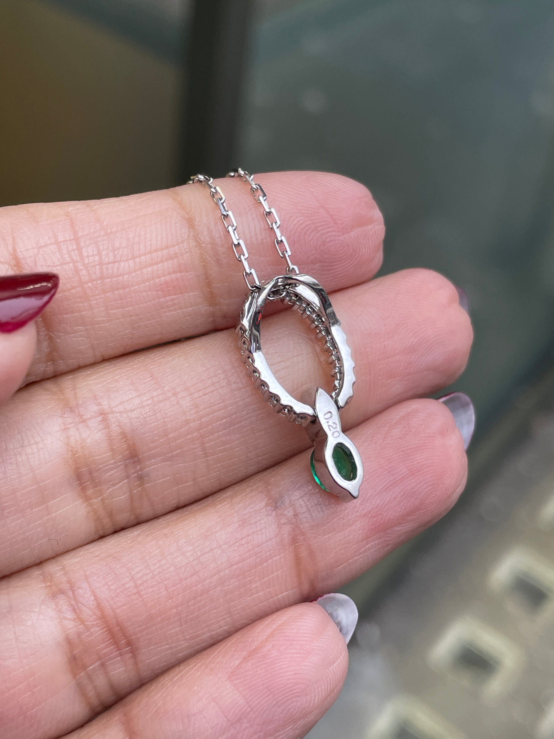 An 18 carat white gold oval pendant featuring a central emerald, surrounded by round brilliant cut diamonds set in a claw-like design.