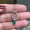 An 18 carat white gold oval pendant featuring a central emerald, surrounded by round brilliant cut diamonds set in a claw-like design.