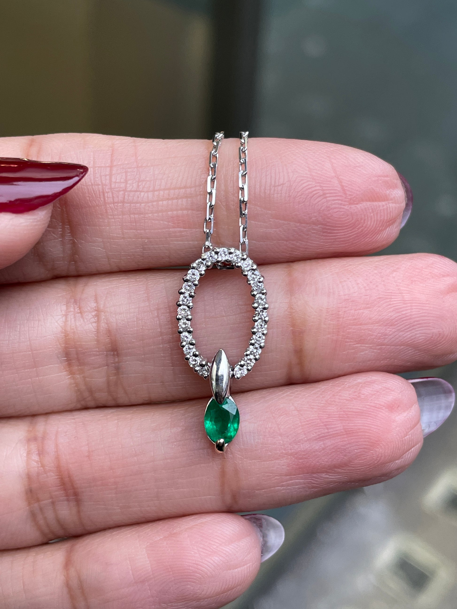 An 18 carat white gold oval pendant featuring a central emerald, surrounded by round brilliant cut diamonds set in a claw-like design.