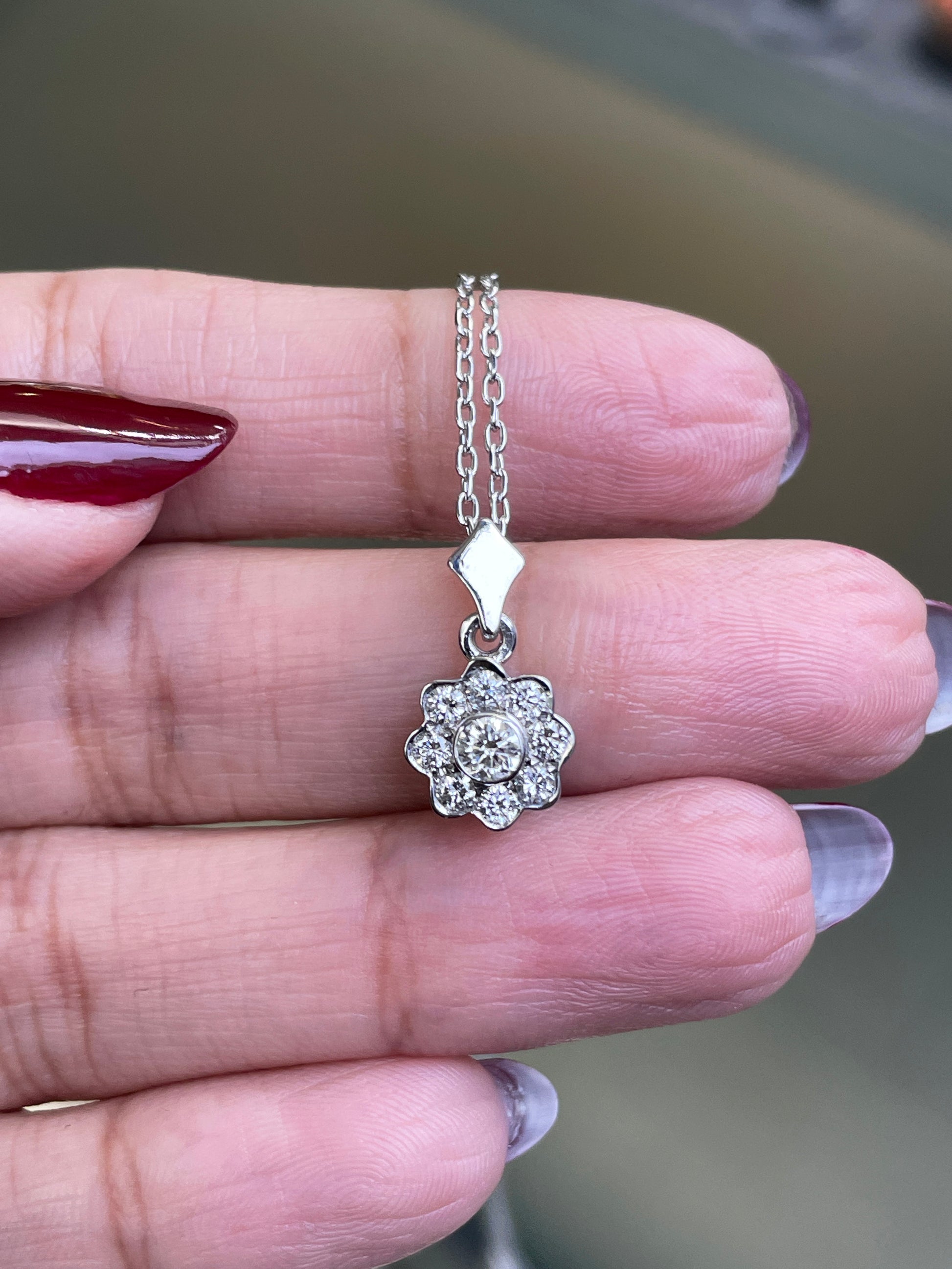 0.45 carat diamond flower cluster pendant crafted in 18 carat white gold, round brilliant cut diamonds arranged in a floral design, suspended from a delicate white gold chain. on hand
