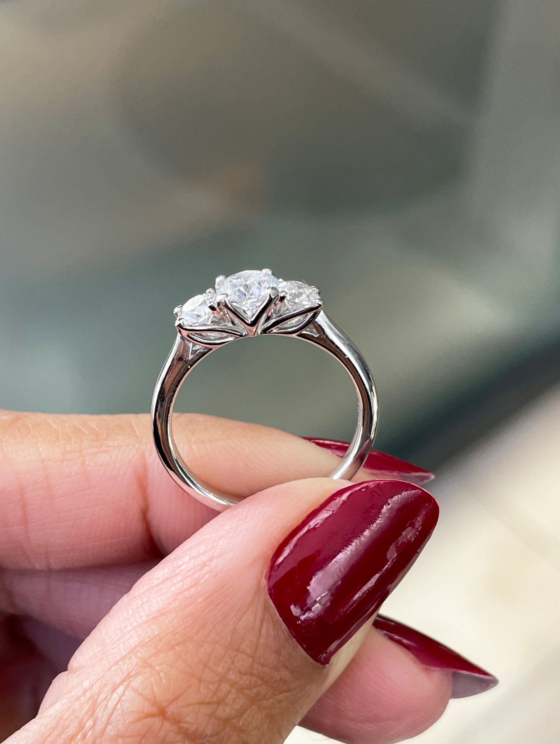 A platinum engagement ring with a central round brilliant cut diamond and two smaller round cut diamonds on the sides, set in an open work gallery on hand.