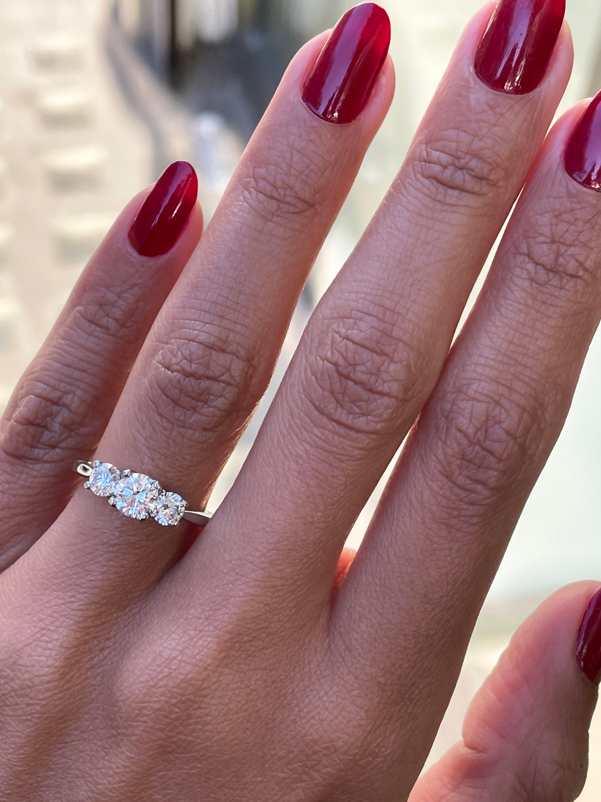 A platinum engagement ring with a central round brilliant cut diamond and two smaller round cut diamonds on the sides, set in an open work gallery on hand.