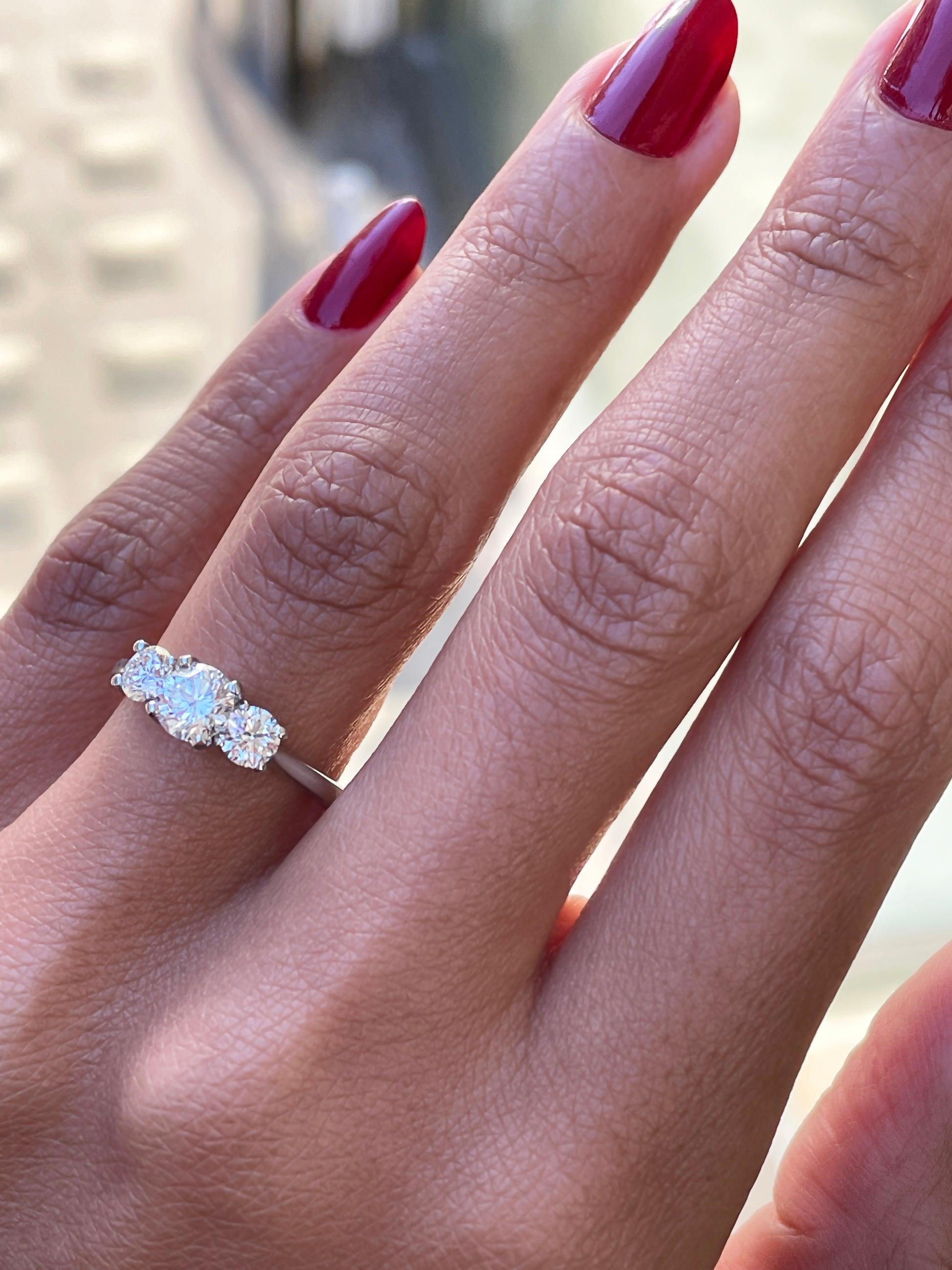A platinum engagement ring with a central round brilliant cut diamond and two smaller round cut diamonds on the sides, set in an open work gallery on hand.