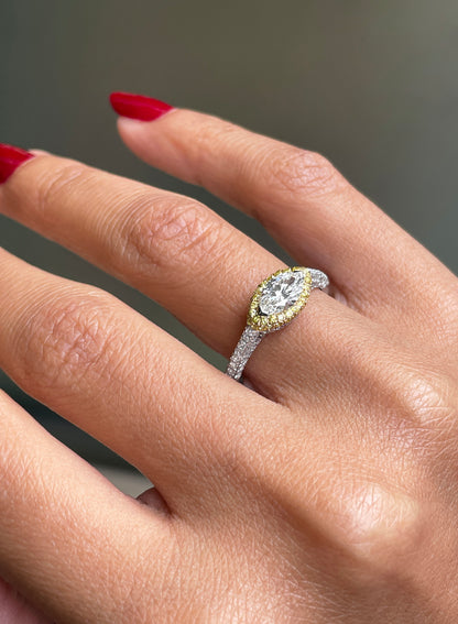 A marquise diamond engagement ring with an east west setting  halo of round yellow diamonds set in rose gold, with smaller white round brilliant cut diamonds set in a contrasting band of platinum. side view