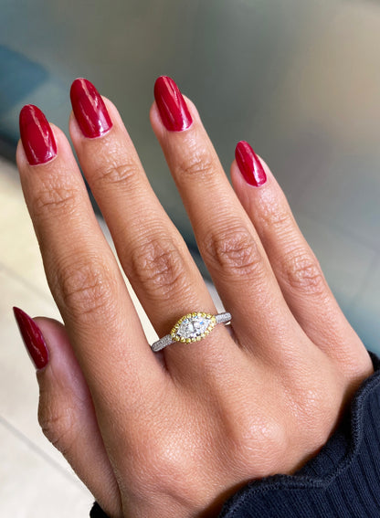 A marquise diamond engagement ring with an east west setting  halo of round yellow diamonds set in rose gold, with smaller white round brilliant cut diamonds set in a contrasting band of platinum. on hand