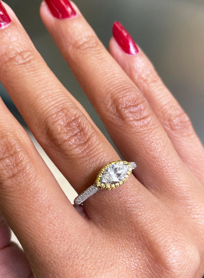 A marquise diamond engagement ring with an east west setting  halo of round yellow diamonds set in rose gold, with smaller white round brilliant cut diamonds set in a contrasting band of platinum. on hand