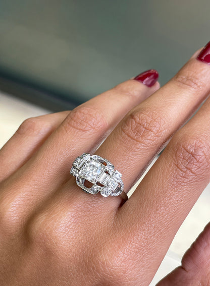 An Art Deco style engagement ring with a central old cut diamond and additional diamonds set in a platinum mount with open work detailing on hand