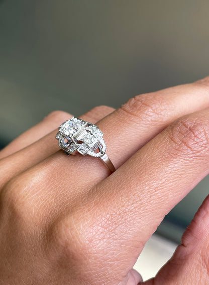 An Art Deco style engagement ring with a central old cut diamond and additional diamonds set in a platinum mount with open work detailing on hand