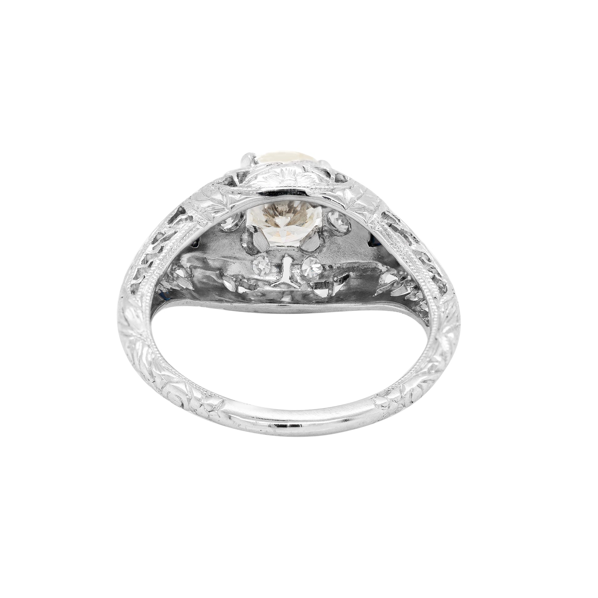 A hand-carved platinum engagement ring with a round brilliant cut diamond centerpiece, accompanied by two triangle-shaped sapphires and six grain-set diamonds 