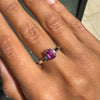 Hand wearing a ring with a pink sapphire on a neutral background