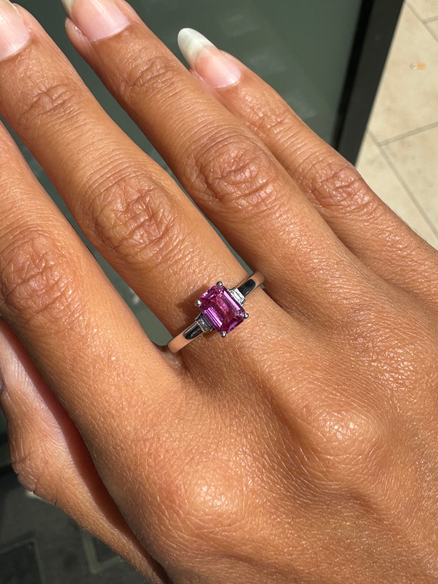 Hand wearing a ring with a pink sapphire on a neutral background