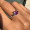 pink sapphire ring on a finger with a blurred background