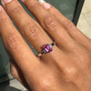Hand wearing a ring with a pink sapphire on a neutral background